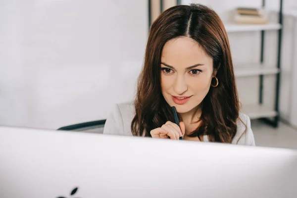 Attentive, beautiful, secretary looking at computer monitor while sitting at workplace — Stock Photo