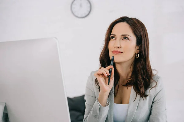 Beautiful, dreamy secretary looking away and holding pen while sitting at workplace — Stock Photo