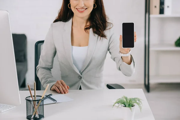 Ausschnitt der Sekretärin zeigt Smartphone mit leerem Bildschirm, während sie am Arbeitsplatz sitzt — Stockfoto