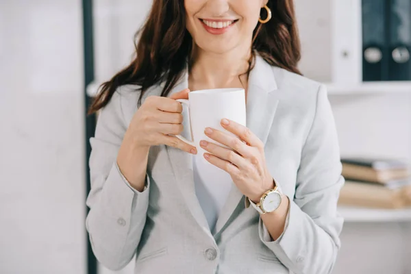 Vista recortada de la sonriente secretaria sosteniendo taza de café en la oficina - foto de stock