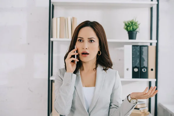 Geschockte Sekretärin zeigt Achselzucken-Geste beim Gespräch auf Smartphone im Büro — Stockfoto