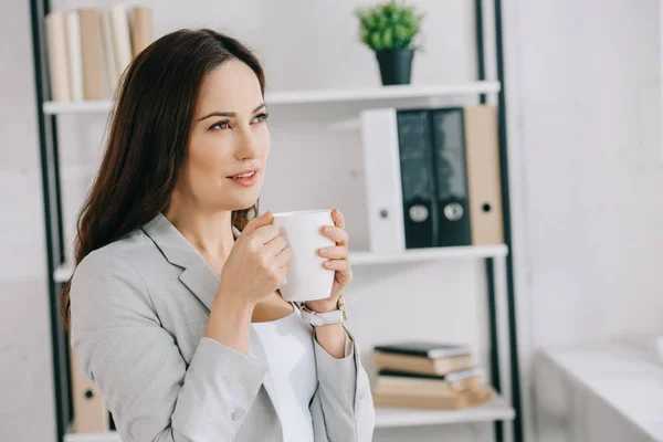 Красивая, задумчивая секретарша смотрит в сторону, держа чашку кофе — стоковое фото