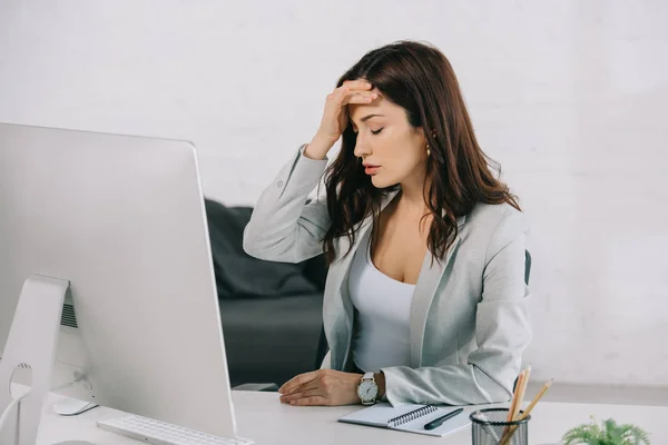 Exhausted secretary suffering from headache while sitting with closed eyes and holding hand near head — Stock Photo