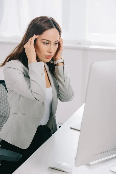 Exhausted secretary holding hands near head while sitting at workplace and suffering from headache — Stock Photo