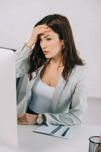 Agotado secretario sosteniendo la mano cerca de la cabeza mientras está sentado en el lugar de trabajo y sufriendo de dolor de cabeza - foto de stock