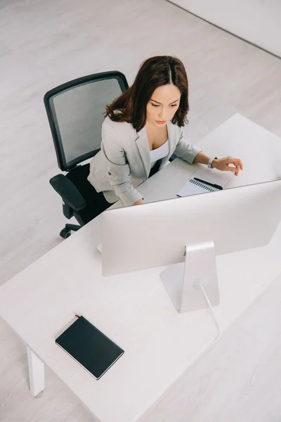 Blick aus der Vogelperspektive auf eine junge, aufmerksame Sekretärin, die am Arbeitsplatz im Büro sitzt — Stockfoto