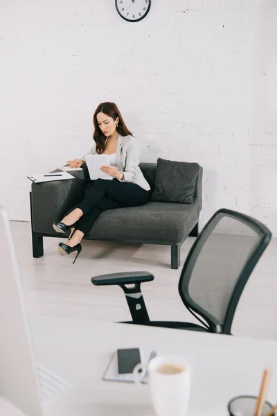 Selective focus of elegant secretary working while sitting on couch in office — Stock Photo