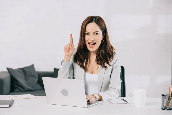 Aufgeregte junge Sekretärin zeigt Ideenschild, während sie am Arbeitsplatz im Büro sitzt — Stockfoto