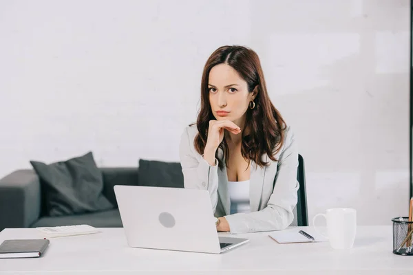 Pensive young secretary looking at camera while sitting at workplace in office — Stock Photo