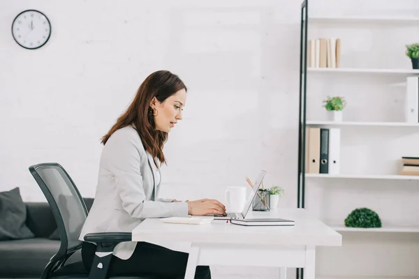 Atento, joven secretaria usando el ordenador portátil mientras está sentado en el lugar de trabajo en la oficina — Stock Photo