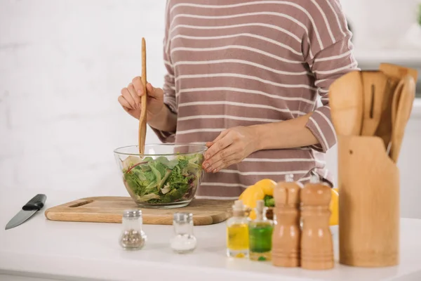 Cropped view of woman mixing fresh vegetable salad while standing at kitchen table — Stock Photo