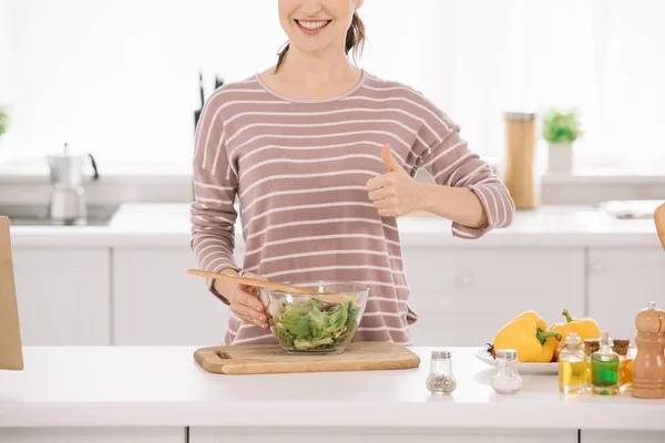 Vista recortada de la mujer sonriente mostrando el pulgar hacia arriba mientras está de pie cerca del tazón con ensalada de verduras frescas - foto de stock