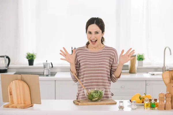 Aufgeregte junge Frau zeigt Wow-Geste, während sie neben Schüssel mit frischem Gemüsesalat steht — Stockfoto