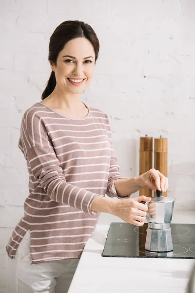 Молодая, веселая женщина, глядя в камеру во время подготовки кофе в гейзер кофеварка — стоковое фото