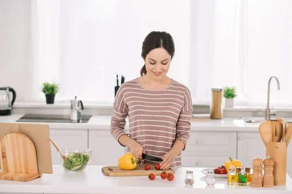 Привлекательная, улыбающаяся женщина режет свежие овощи на доске — стоковое фото