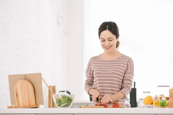 Atractiva, mujer alegre cortar verduras frescas en la tabla de cortar - foto de stock