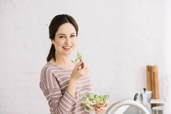 Jovem, mulher sorridente olhando para a câmera enquanto come salada de legumes — Fotografia de Stock