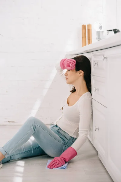 Femme au foyer fatiguée assise sur le sol dans la cuisine avec les yeux fermés — Photo de stock