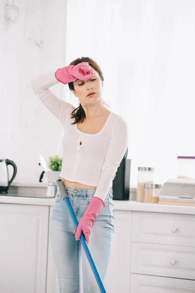 Femme au foyer fatiguée tenant la main près de la tête tout en se tenant dans la cuisine — Photo de stock