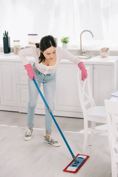 Joven ama de casa en azul jeans lavando piso en cocina con fregona - foto de stock