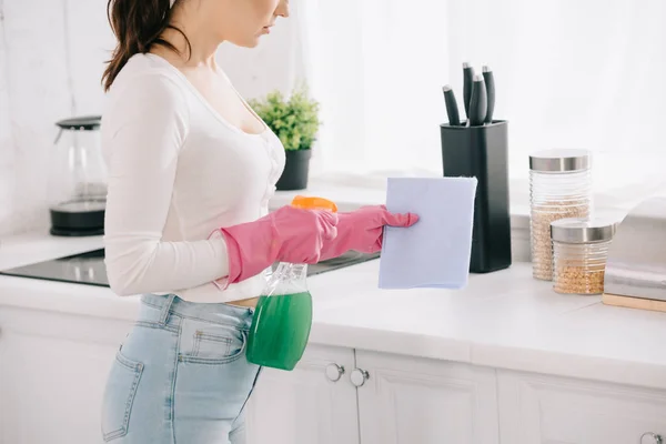Vista cortada de dona de casa segurando spray garrafa e pano na cozinha — Fotografia de Stock