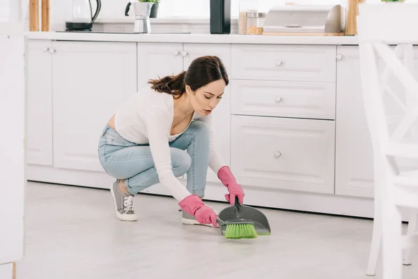 Attractive, young housewife sweeping floor with brush and scoop — Stock Photo