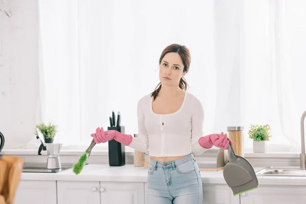 Dona de casa pensativa segurando colher e escova enquanto olha para a câmera na cozinha — Fotografia de Stock