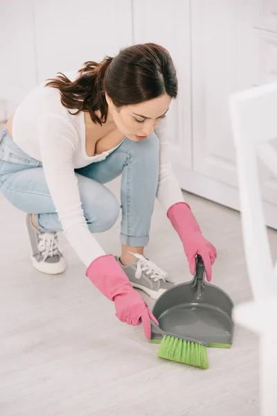 Jeune femme au foyer balayage étage dans la cuisine avec brosse et scoop — Photo de stock