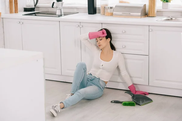 Exhausted housewife sitting on floor in kitchen near scoop and brush — Stock Photo