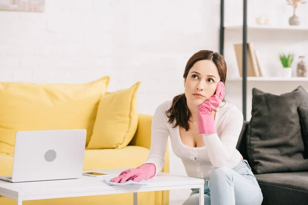 Pensive housewife talking on smartphone while wiping table with rag — Stock Photo
