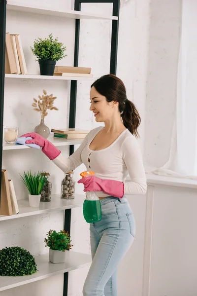 Feliz ama de casa estante de limpieza con trapo y la celebración de botella de spray con detergente - foto de stock