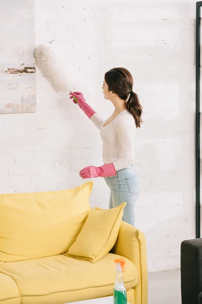 Jeune femme au foyer nettoyage photo sur le mur avec brosse à épousseter — Photo de stock