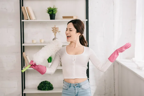 Fröhliche Hausfrau singt mit Staubwedel, während sie am Regal steht — Stockfoto