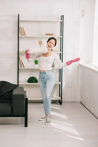 Fröhliche Hausfrau, die im Wohnzimmer mit Staubwedel singt — Stockfoto