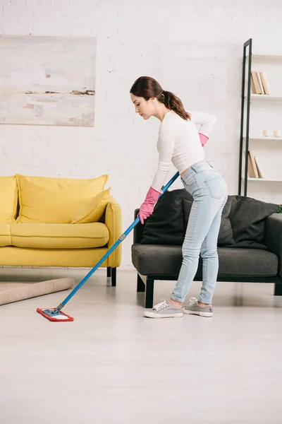 Молода домогосподарка миє підлогу з мопедом біля жовтих і сірих диванів — стокове фото