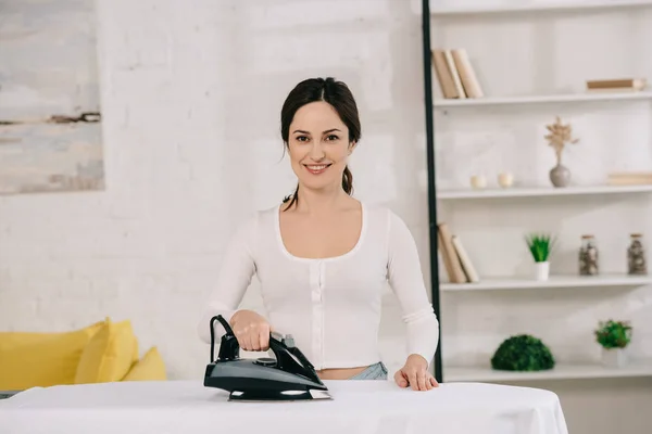 Allegra casalinga sorridente alla macchina fotografica mentre stiratura su asse da stiro — Foto stock