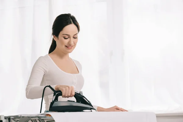 Joven ama de casa sonriendo mientras plancha en tabla de planchar — Stock Photo