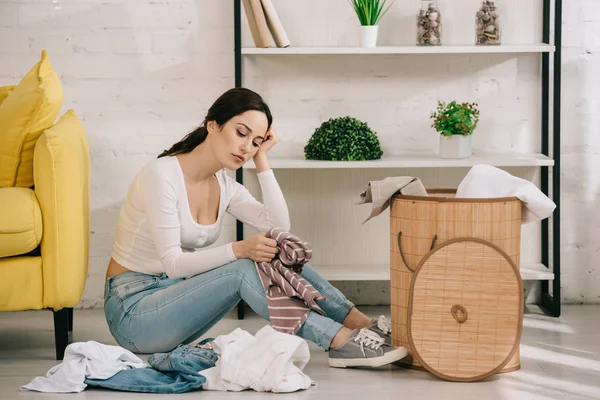 Tired housewife sitting on floor near clothes and laundry basket — Stock Photo