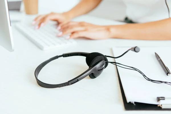 Foco seletivo do fone de ouvido preto perto de digitação corretor no teclado do computador no escritório — Fotografia de Stock