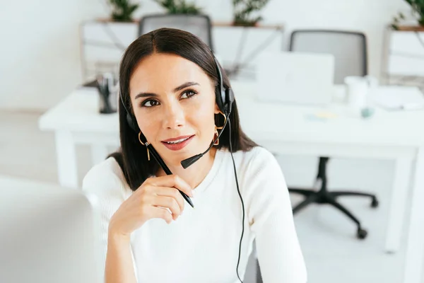 Selective focus of pensive broker in headset holding pen in office — Stock Photo