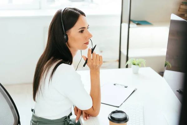 Attraktiver Makler im Headset, der in der Nähe von Pappbechern im Amt hält — Stockfoto