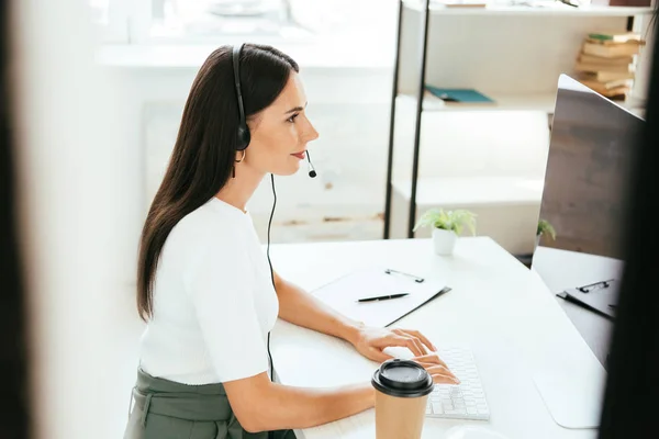 Selective focus of happy broker in headset typing on computer keyboard in office — Stock Photo
