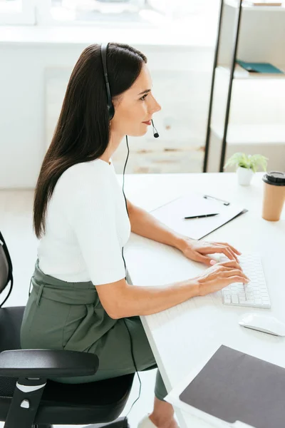 Felice broker in cuffia digitando sulla tastiera del computer in ufficio — Foto stock