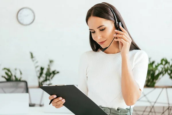 Sorridente broker toccando auricolare tenendo appunti — Foto stock