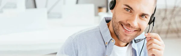 Panoramic shot of happy operator in brokers agency touching headset and looking at camera — Stock Photo