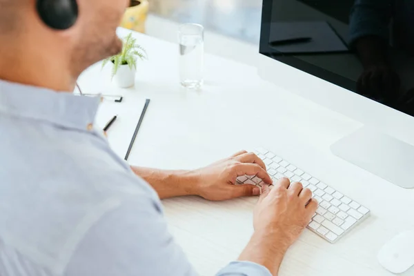 Enfoque selectivo del corredor de escribir en el teclado de la computadora cerca del monitor de la computadora con pantalla en blanco - foto de stock