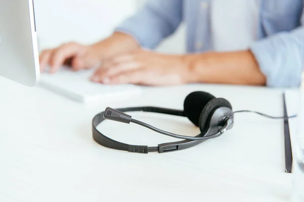 Messa a fuoco selettiva di auricolare nero vicino operatore in intermediari agenzia digitando in ufficio — Foto stock
