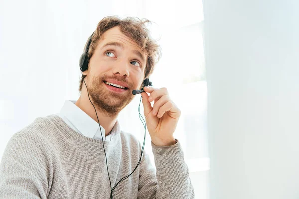 Bonito operador barbudo em corretores agência sorrindo e tocando fone de ouvido — Stock Photo