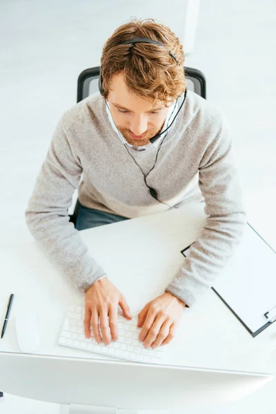 Top view of bearded broker in headset typing on computer keyboard — Stock Photo