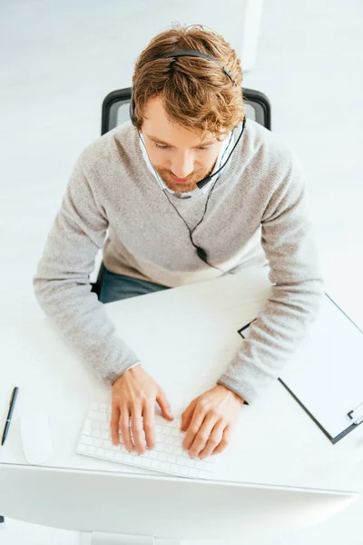 Vue du haut du courtier barbu dans la saisie du casque sur le clavier de l'ordinateur — Photo de stock